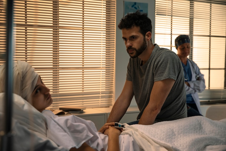 Man comforting a patient in a hospital bed, with a nurse observing in the background, illustrating compassionate care in a medical setting.